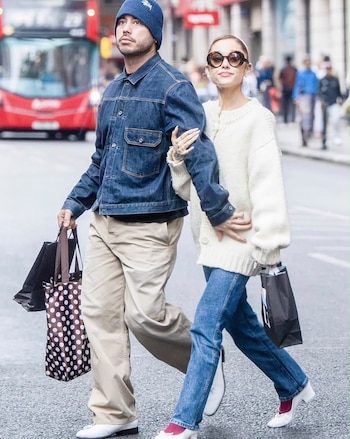 Ariana Grande con gafas de sol y suéter claro camina tomada del brazo de Ricky Alvarez por una calle