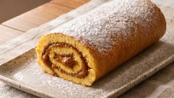 Doce de leite de leite integral polvilhado com açúcar de confeiteiro, em prato retangular. Você pode ver as camadas que enrolaram o bolo e o recheio cor de caramelo.