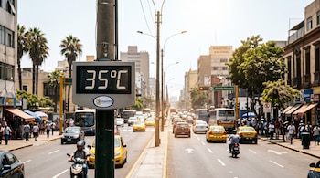 Termómetro digital en un poste que marca 35 grados Celsius frente al tránsito vehicular de una avenida con edificios y peatones.