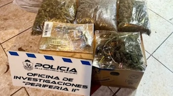 Múltiples bolsas transparentes con marihuana y un paquete envuelto en papel plateado, junto a un cartel de la Policía de Neuquén en un suelo de baldosas