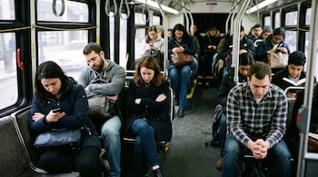 Pasajeros sentados dentro de un autobús público miran sus teléfonos móviles, leen o permanecen con los brazos cruzados.