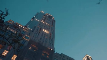 Vista de ángulo bajo de un rascacielos moderno con ventanas iluminadas contra un cielo azul oscuro al anochecer, con otros edificios parcialmente visibles