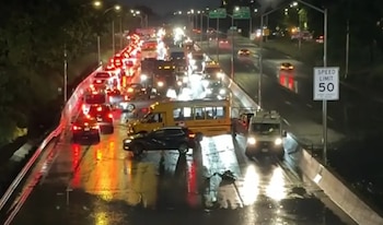 Vista aérea nocturna de una autopista con tráfico pesado y carriles inundados; coches y un autobús escolar están atrapados en el agua estancada