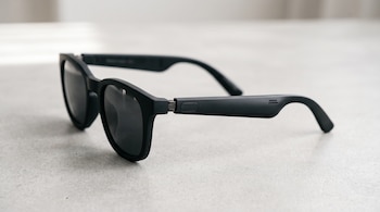 Gafas de sol inteligentes de color negro mate con un botón lateral sobre una superficie gris clara.