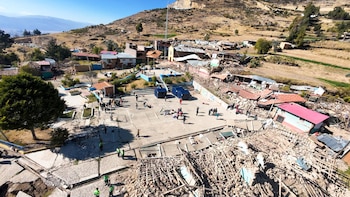 Vista aérea de un pueblo afectado por un sismo con casas colapsadas, escombros, personas reunidas en una plaza y dos carpas azules