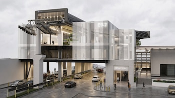 Edificio de cristal y acero etiquetado como Estación 2, sobre una calle con autos y una cabina verde de teleférico en la parte superior