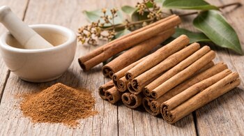 Palos de canela, canela en polvo, mortero de cerámica con pistilo, hojas y ramas de planta, y superficie de madera.