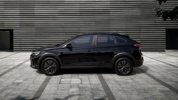 Vista lateral de un vehículo Volkswagen Nivus negro brillante estacionado sobre un pavimento de baldosas grises, frente a una pared moderna con franjas horizontales oscuras