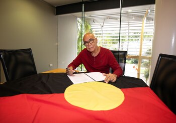 HANDOUT - El artista Harold Thomas, creador en 1970 de la bandera aborigen australiana, en momentos en que firma un acuerdo de cesión de derechos con la Mancomunidad de Naciones en oficinas de la Agencia Nacional Indígena de Australia (NIAA). Foto: David Hancock/GRACosway/dpa - ATENCIÓN: Sólo para uso editorial en relación con la cobertura sobre (la emisión/la película/la subasta/la exposición/el libro) y mencionando el crédito completo