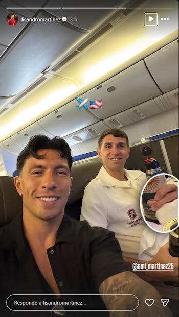 Primer plano de Lisandro Martínez sonriendo a cámara, con Dibu Martínez sonriendo detrás y sosteniendo un termo con un mate en un avión
