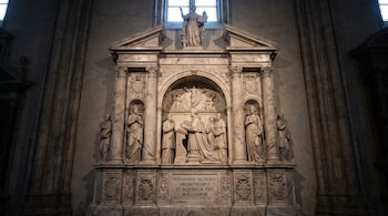 Monumento funerario de alabastro con esculturas de figuras orantes, relieves religiosos, columnas y una estatua en la cúspide.