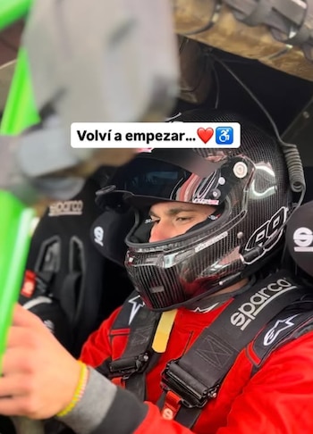 Persona con casco negro, traje de carreras rojo y arnés de seguridad al volante dentro del habitáculo de un automóvil de competición