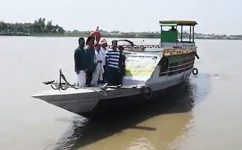 Un barco de madera con varios hombres sobre la cubierta navega por un río cerca de la orilla