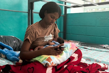 Eliana García, de 19 años, revisa su teléfono móvil mientras amamanta a su bebé Gael Jesús —nacido en La Guaira un día después de los terremotos del 24 de junio— en un refugio de la Escuela Bolivariana 10 de Marzo en Maiquetía, estado de La Guaira, Venezuela, el 7 de julio de 2026 (Paula Ramon/AFP)