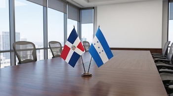 Dos pequeñas banderas de mesa de la República Dominicana y Honduras colocadas juntas sobre una mesa de madera en una sala de conferencias.