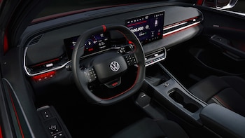 Interior de un Volkswagen ID.Polo GTI con volante de cuero negro y costuras rojas, salpicadero digital con dos pantallas, y consola central en tonos oscuros