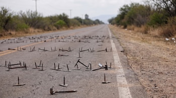 Decenas de picos metálicos artesanales se encuentran esparcidos sobre el asfalto de un camino rodeado de vegetación.