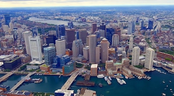 Vista aérea de Boston, EEUU, con numerosos rascacielos marrones y grises, un río y un puerto con barcos, y puentes sobre el agua bajo un cielo nublado