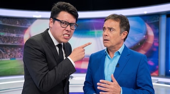 Dos hombres en un estudio de televisión. Uno con traje oscuro, gafas, apunta con el dedo. El otro, con traje azul, tiene las manos juntas y rostro sorprendido.