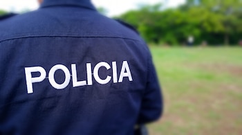 Uniforme azul escuro com a palavra 'POLÍCIA' bordada em branco nas costas, com uma planta verde clara.