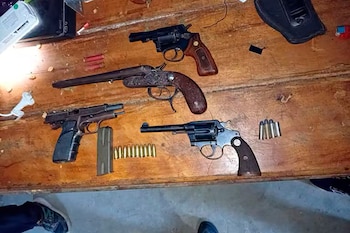 Cuatro armas de fuego, incluyendo revólveres, una pistola y una escopeta recortada, junto a municiones de diferentes calibres, sobre una superficie de madera