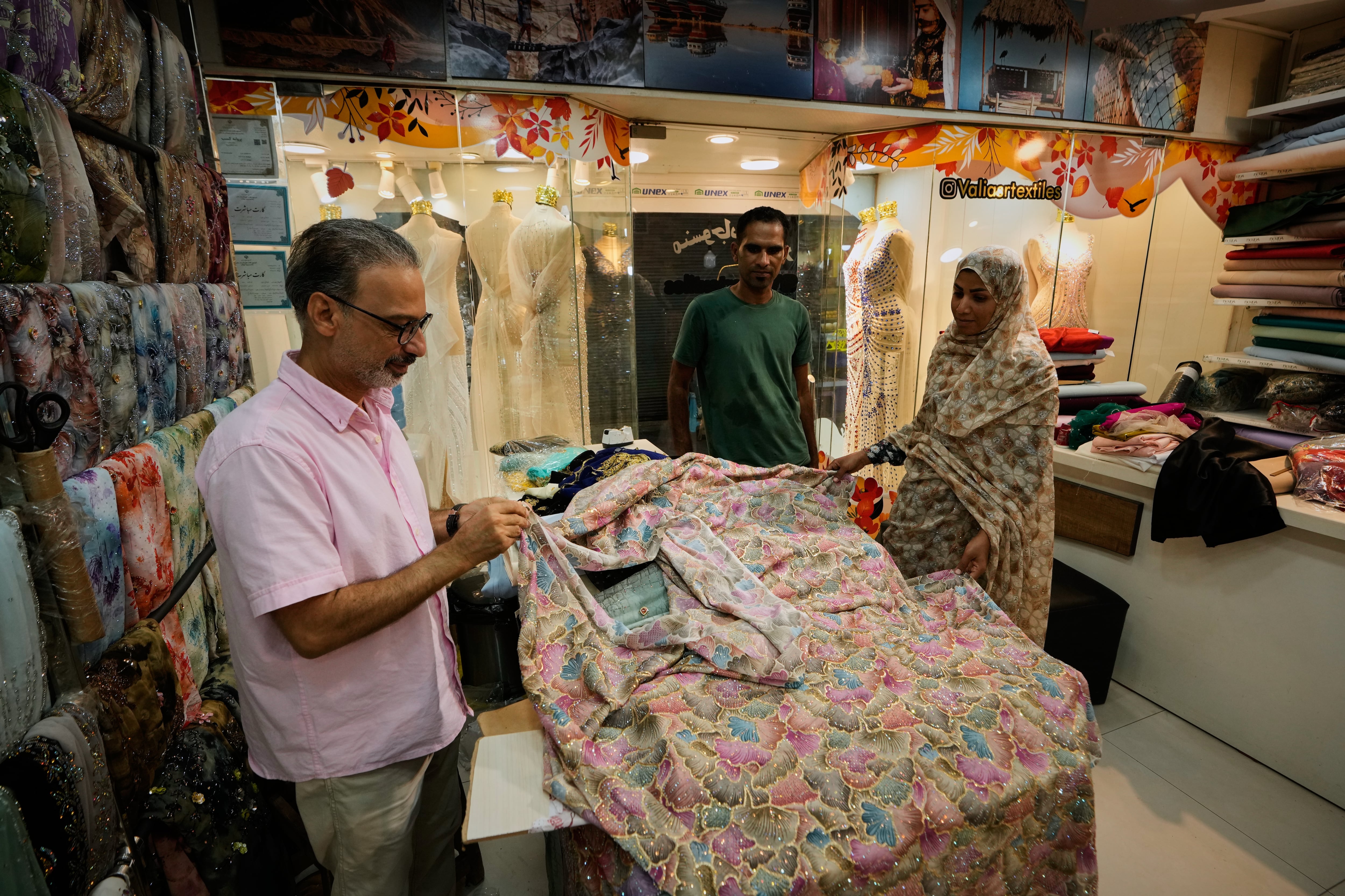Unas personas examinan telas bordadas en una tienda de textiles de un bazar tradicional en Bandar Abbas, Irán, el domingo 6 de septiembre de 2026 (AP/Vahid Salemi)