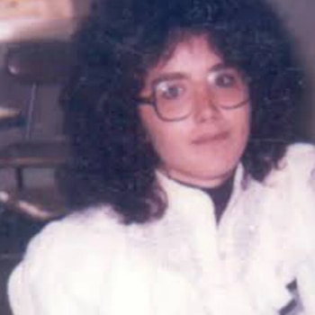 Fotografía de una mujer con cabello oscuro y rizado, usa gafas y lleva una camisa blanca o de color claro