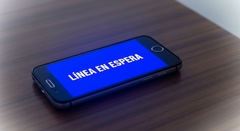 Teléfono celular apoyado en mesa de madera con la pantalla azul encendida, que muestra las palabras LÍNEA EN ESPERA en letras blancas.