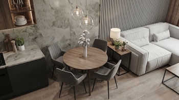 Vista superior de una sala pequeña que integra comedor y sala de estar. Se aprecian un sofá blanco, mesa de madera, sillas grises, lámparas colgantes, y paredes texturizadas.