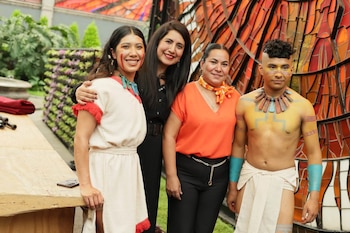 Cuatro personas posan juntas frente a una estructura de vitral; dos de ellas llevan ropa de estilo indígena y pintura facial