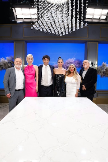 Tres hombres y tres mujeres posan de pie detrás de una mesa blanca de mármol en un estudio de televisión con fondo azul