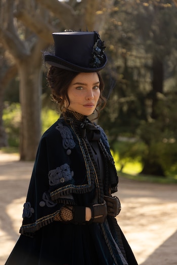 Retrato de mujer con cabello oscuro, ojos claros, sombrero de copa oscuro con velo, vestido de terciopelo azul marino con adornos y guantes negros