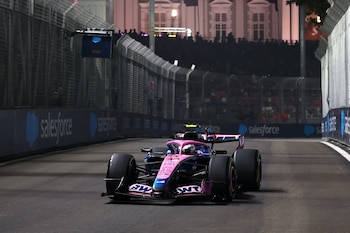 Un monoplaza de carreras rosa y azul avanza por un circuito urbano delimitado por vallas metálicas bajo iluminación nocturna