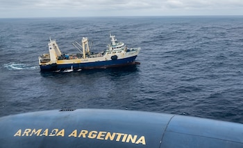 Un buque pesquero blanco y azul, con la identificación VJRN4, navega en aguas onduladas bajo un cielo nublado, visto desde la proa de un buque de la Armada Argentina