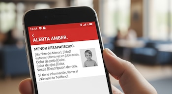 Primer plano de una mano sosteniendo un smartphone que muestra una Alerta Amber en español con la foto de un niño y texto "Menor Desaparecido" en la pantalla.