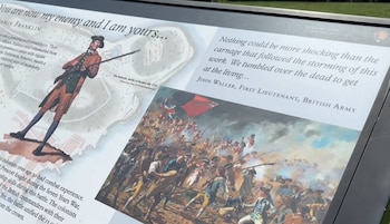 Primer plano de un panel informativo al aire libre sobre la Batalla de Bunker Hill, con ilustraciones de soldados y mapas, y texto histórico