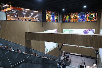 Interior renovado de la estación Auditorio del Metro CDMX, mostrando escaleras, paredes de madera, carteles y un vitral colorido en la parte superior, con personas transitando