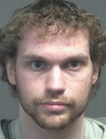 Fotografía de frente de un hombre joven de cabello rizado y barba corta, con ojos claros, mirando directamente a la cámara. Su rostro tiene algunas imperfecciones