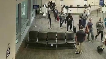 Varias personas con maletas caminan por el pasillo de una terminal cerca de una fila de sillas negras vacías