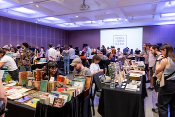 Salón interior con público mirando libros en mesas cubiertas de tela oscura. Al fondo, una pantalla proyecta "Feria Libro Raro"