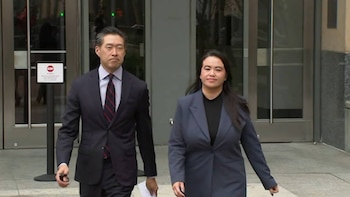 Un hombre con traje y corbata a rayas y una mujer con chaqueta azul caminan frente a la entrada de vidrio de un edificio