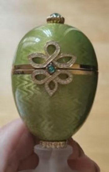 Primer plano de un huevo decorativo verde esmaltado con un patrón ondulado, adornado con un diseño dorado en espiral y gemas centrales