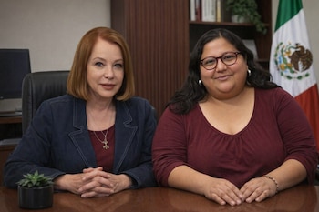 Laura Itzel Castillo y Citlalli Hernández sentadas en un escritorio de madera. Al fondo, una bandera de México y una estantería oscura.