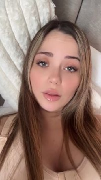 Mujer con cabello castaño y mechas rubias. Tiene ojos claros. Viste una prenda color piel y está recostada. Se observa una almohada blanca