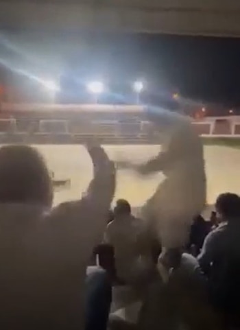 Imagen borrosa nocturna de una multitud con una persona en el aire durante un incidente en un evento al aire libre iluminado por focos