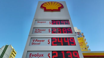 Un cartel de precios digital rojo de una estación de servicio Shell muestra los valores para diferentes tipos de combustible bajo un cielo azul claro