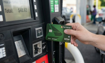 Primer plano de una mano insertando una tarjeta de crédito PNC Bank Visa en un surtidor de gasolina que muestra un total de $48.63 en la pantalla