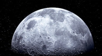 Vista en primer plano de la Luna, que presenta una superficie llena de cráteres y un color gris. Se observa el espacio oscuro con estrellas.