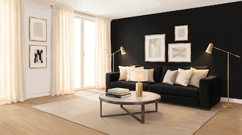 Ilustración de un salón moderno con una pared negra, sofá negro, cojines beige, mesa de centro redonda, lámparas doradas, y cuadros abstractos. Un ventanal con cortinas claras y suelo de madera completa la escena.
