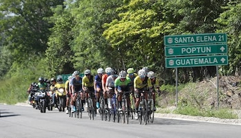 Un ciclista con uniforme negro y amarillo en el centro entre otros ciclistas que sostienen sus bicicletas levantadas sobre la rueda trasera